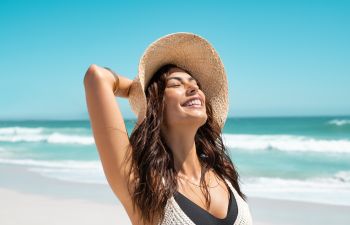 Cheerful beautiful woman with a straw hat enjouying a sunny day on the beach.
