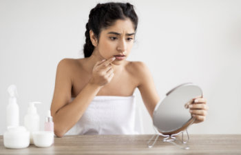 Upset woman touching lips in front of mirror suffering herpes