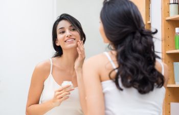 woman stands before a mirror takes care of the skin