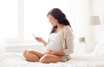 pregnant woman sits on bed and uses phone